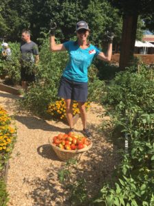 An Extension Master Gardener Volunteer poses excitedly in front of a basket of tomatoes.
