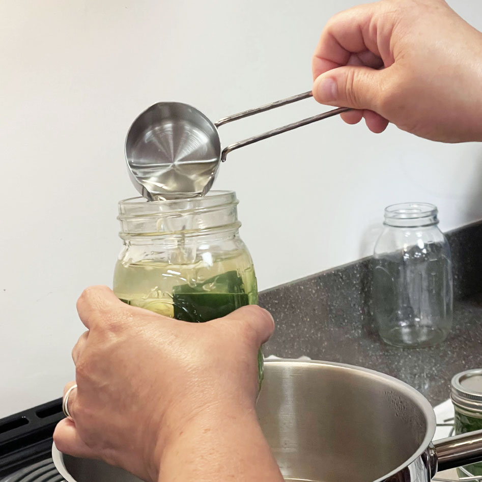 Hot pickling solution being poured over cucumbers in the jars, leaving headspace at the top.